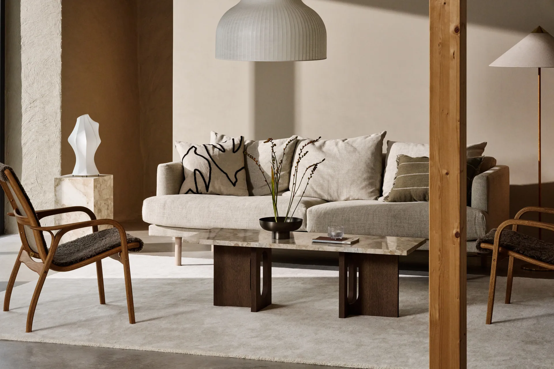 Ett mysigt vardagsrum med ljusbeige soffa, soffbord i marmor, fåtöljer i trä och en ribbad taklampa.