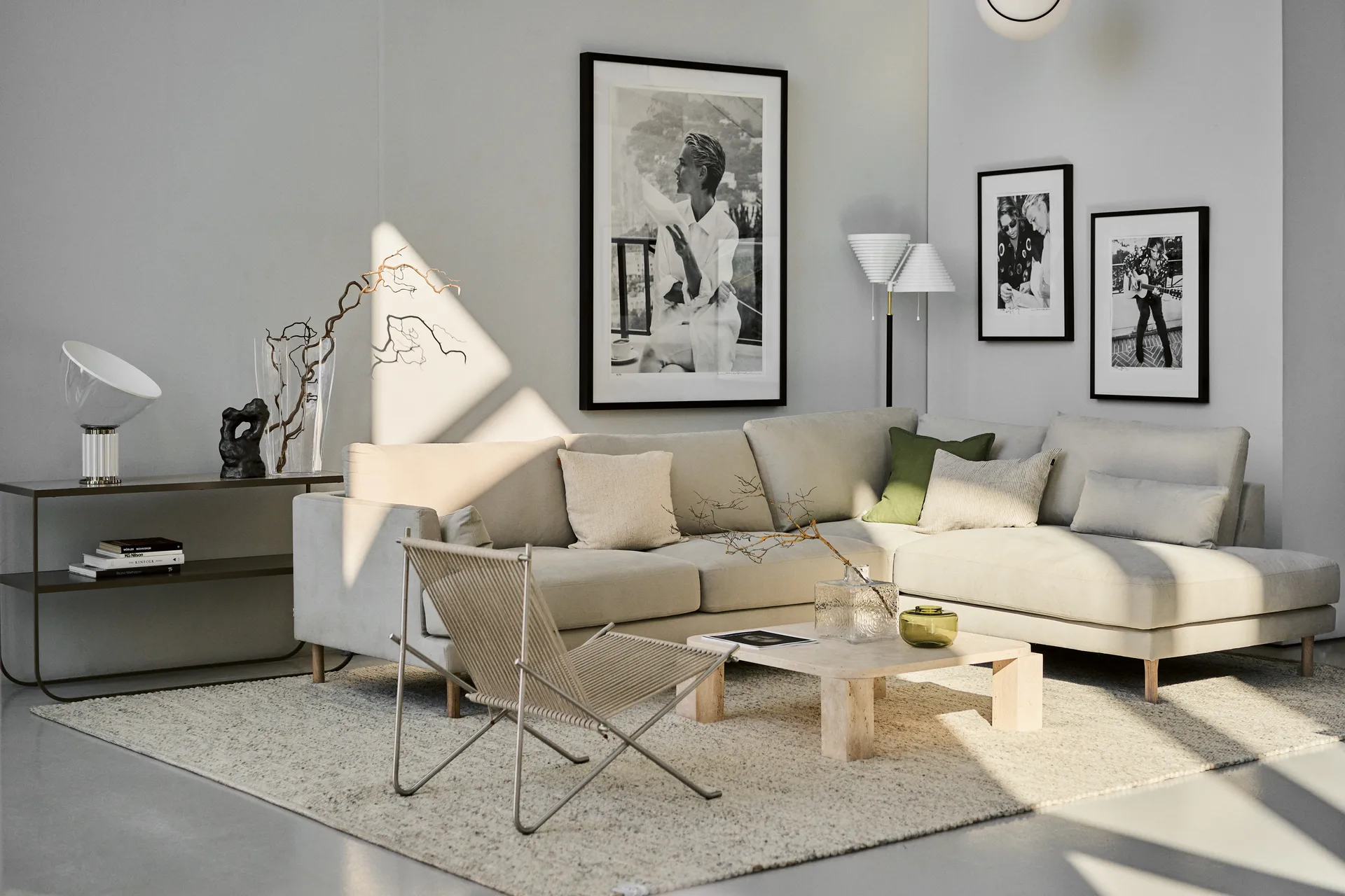 Ett modernt vardagsrum med en ljusbeige hörnsoffa, en flätad stol, en ljus matta och inramad konst.