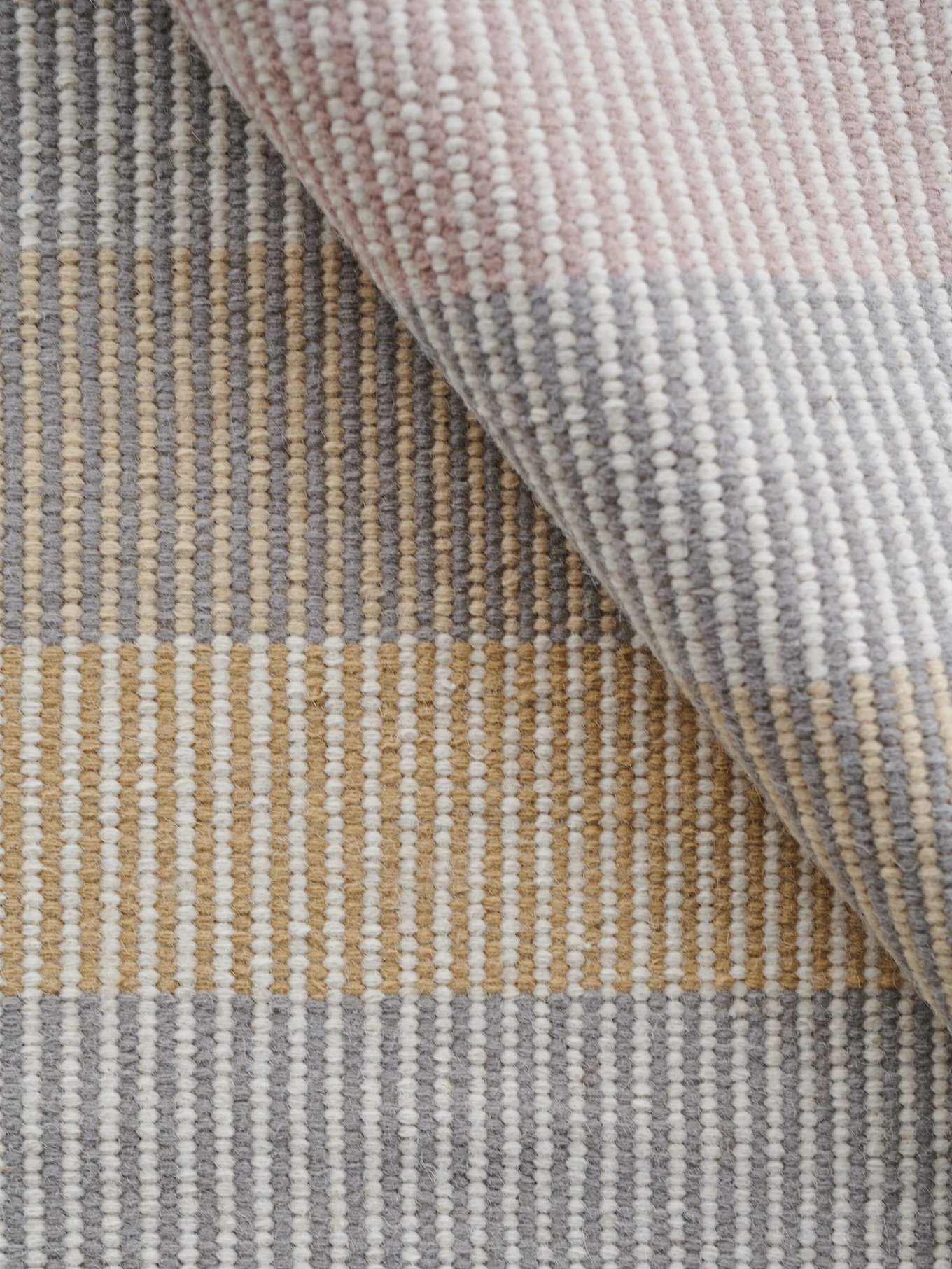 Vävd texturerad matta med vertikala ränder i grått, vitt, beige och ljusrosa, delvis ihoprullad.