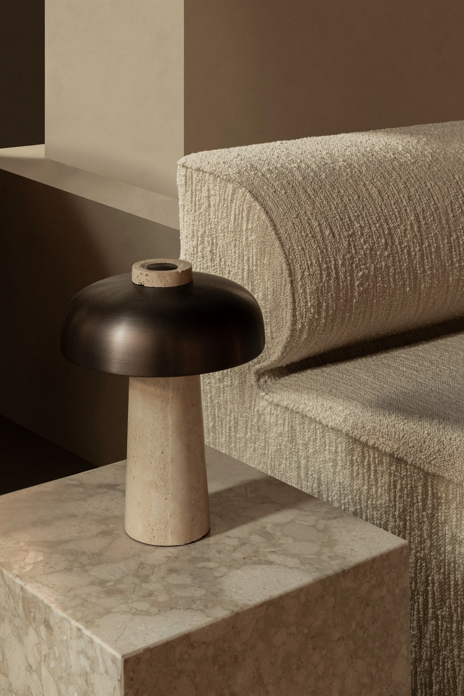 Mörk svampformad bordslampa med beige fot på marmorbord bredvid texturerad beige soffa.
