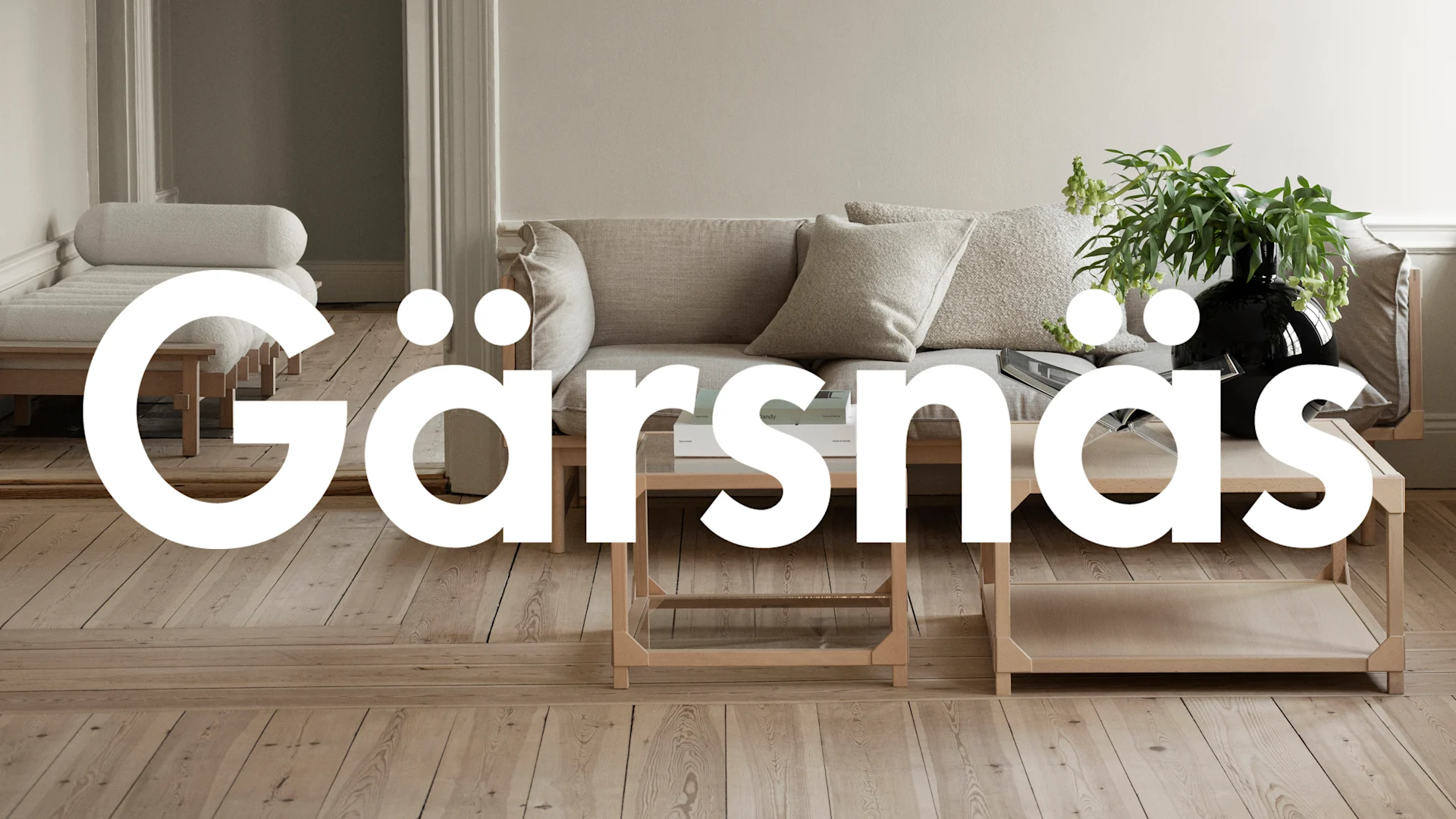 Minimalistiskt vardagsrum med beige soffa, schäslong och ljusa träbord på trägolv. En växt står på ett bord.