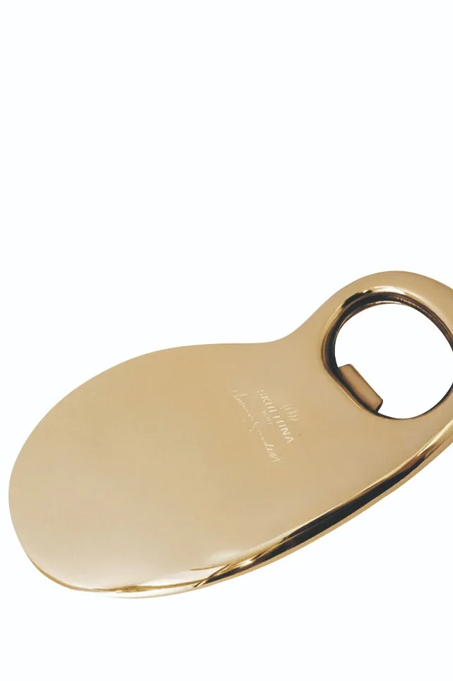 Guldfärgad, oval flasköppnare i polerad metall med en cirkulär öppning i ena änden.
