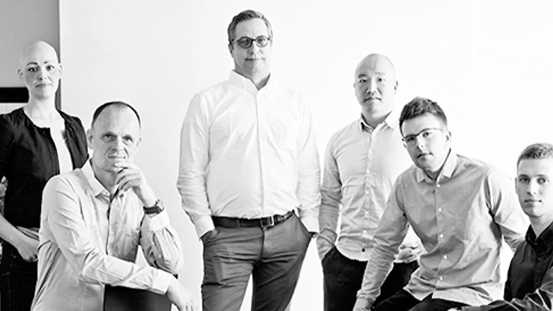 Svartvitt foto av sex personer, fem män och en kvinna, i business casual-kläder, som tittar in i kameran.