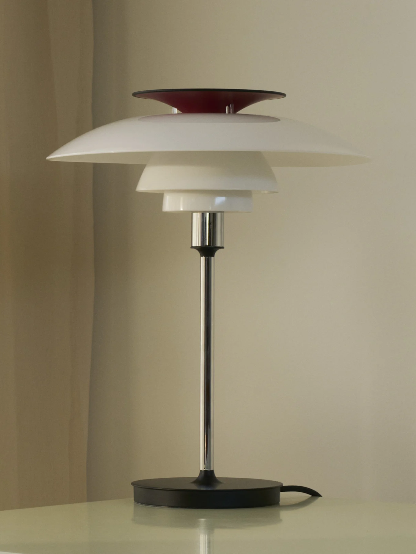 En bordslampa med vita, lagerformade skärmar och en röd topp, på en silverfärgad stång och svart bas.