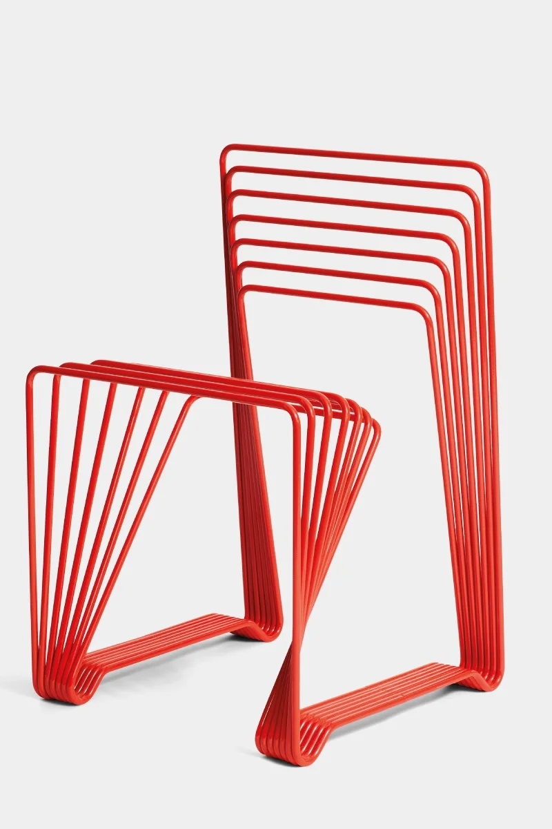 Två röda minimalistiska stolar gjorda av parallella böjda metallrör, en vänd framåt, en i sidled.