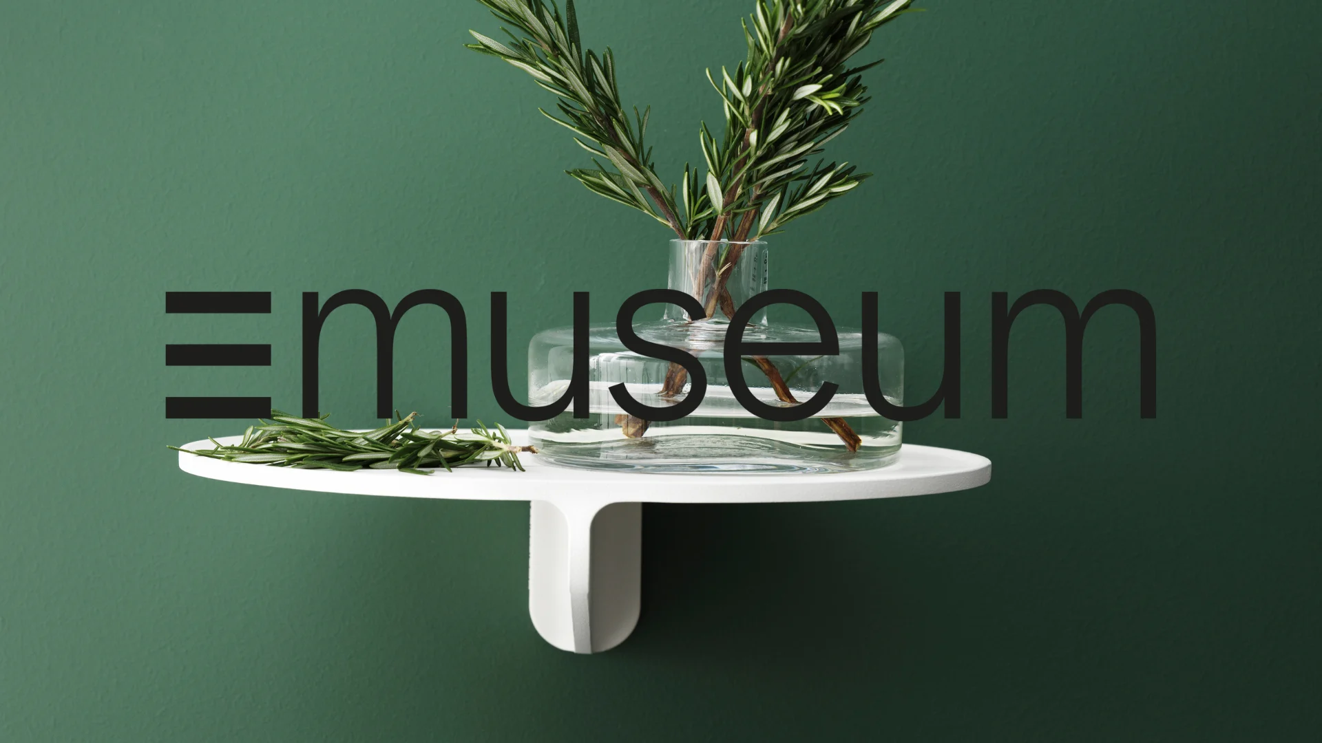En klar glasvas med rosmarin på en vit hylla mot en grön vägg, med texten "emuseum" över bilden.