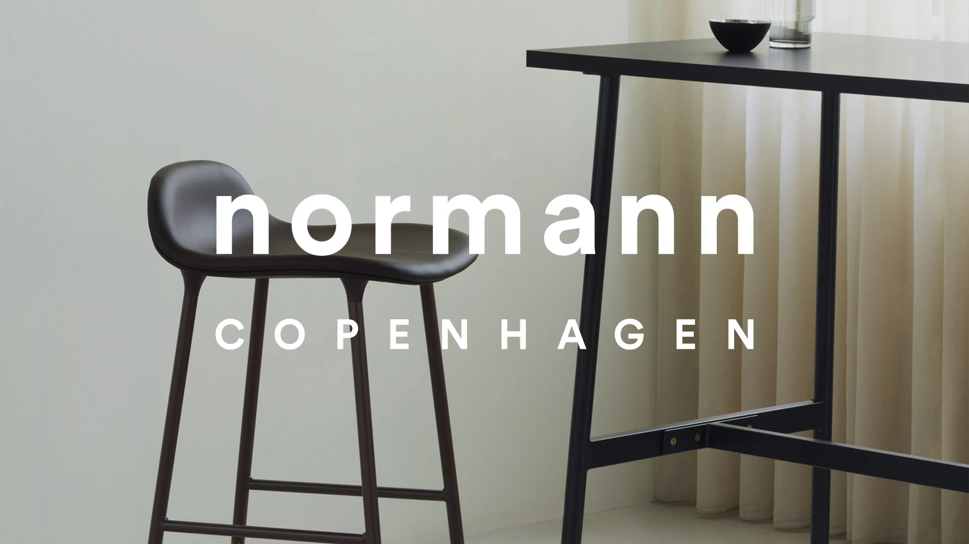 Mörkbrun barpall och svart barbord, med texten ”normann COPENHAGEN” över bilden.