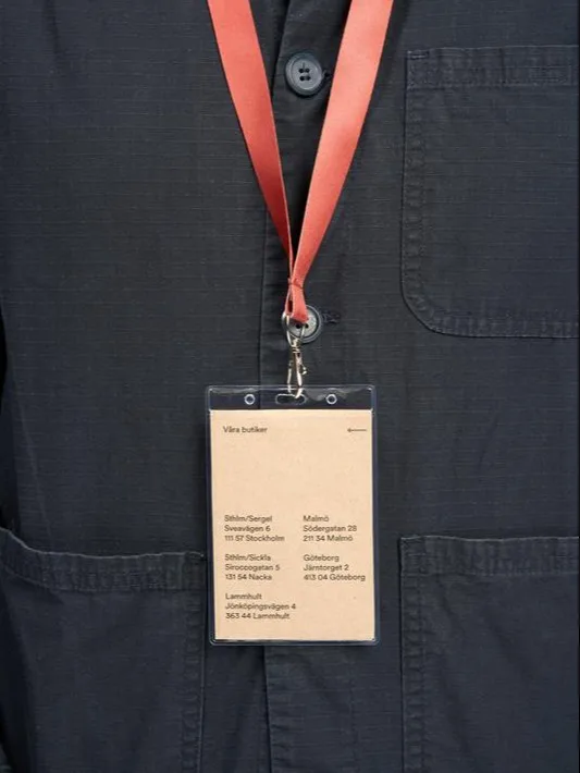 En person i mörkblå skjorta med orange snodd och en namnskylt som visar butiksadresser.