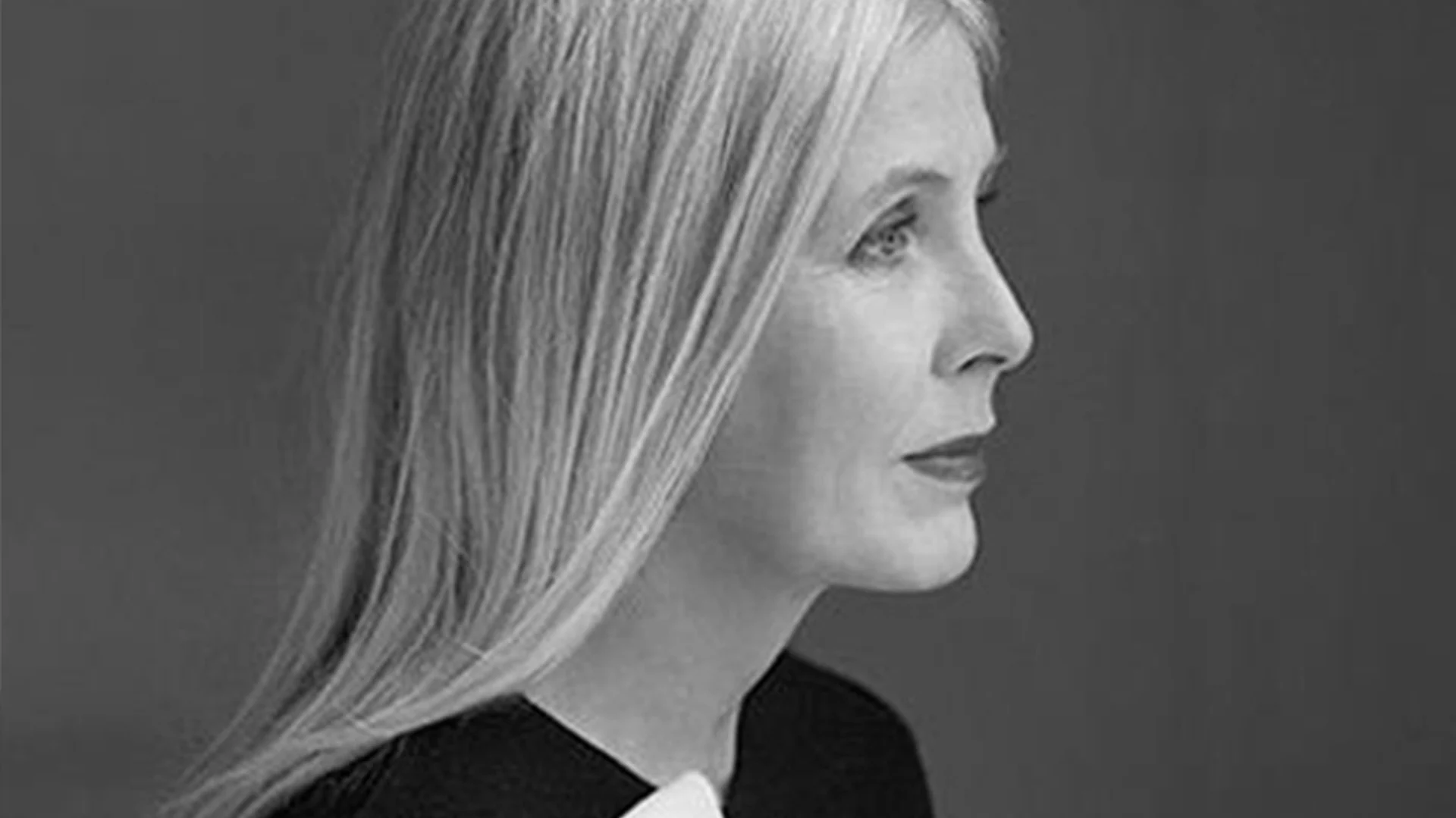 Svartvitt profilfoto av en kvinna med långt blont hår och mörka kläder, som tittar åt höger.