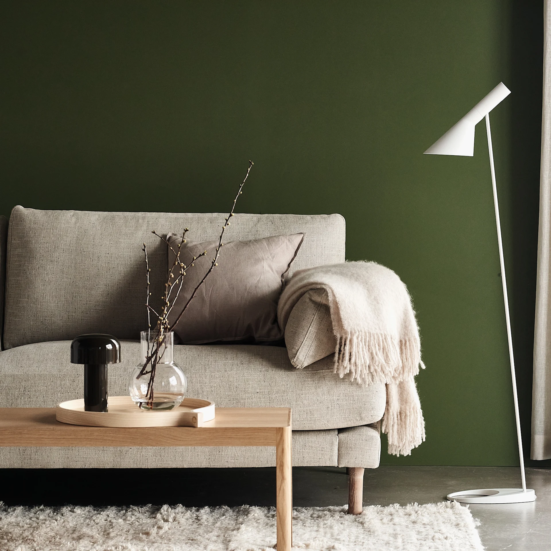 Haga soffa i färgen beige från varumärket 1898, här i grönmålat vardagsrum tillsammans med soffbord i trä och AJ golvlampa i vitt.