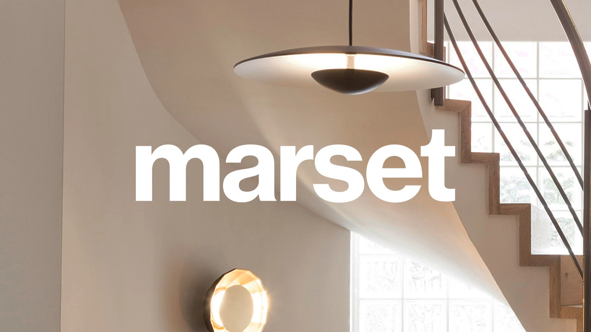 Modern interiör med en mörk, skivformad taklampa och en glödande, texturerad cirkulär vägglampa, med trappa och 'marset'-logga.