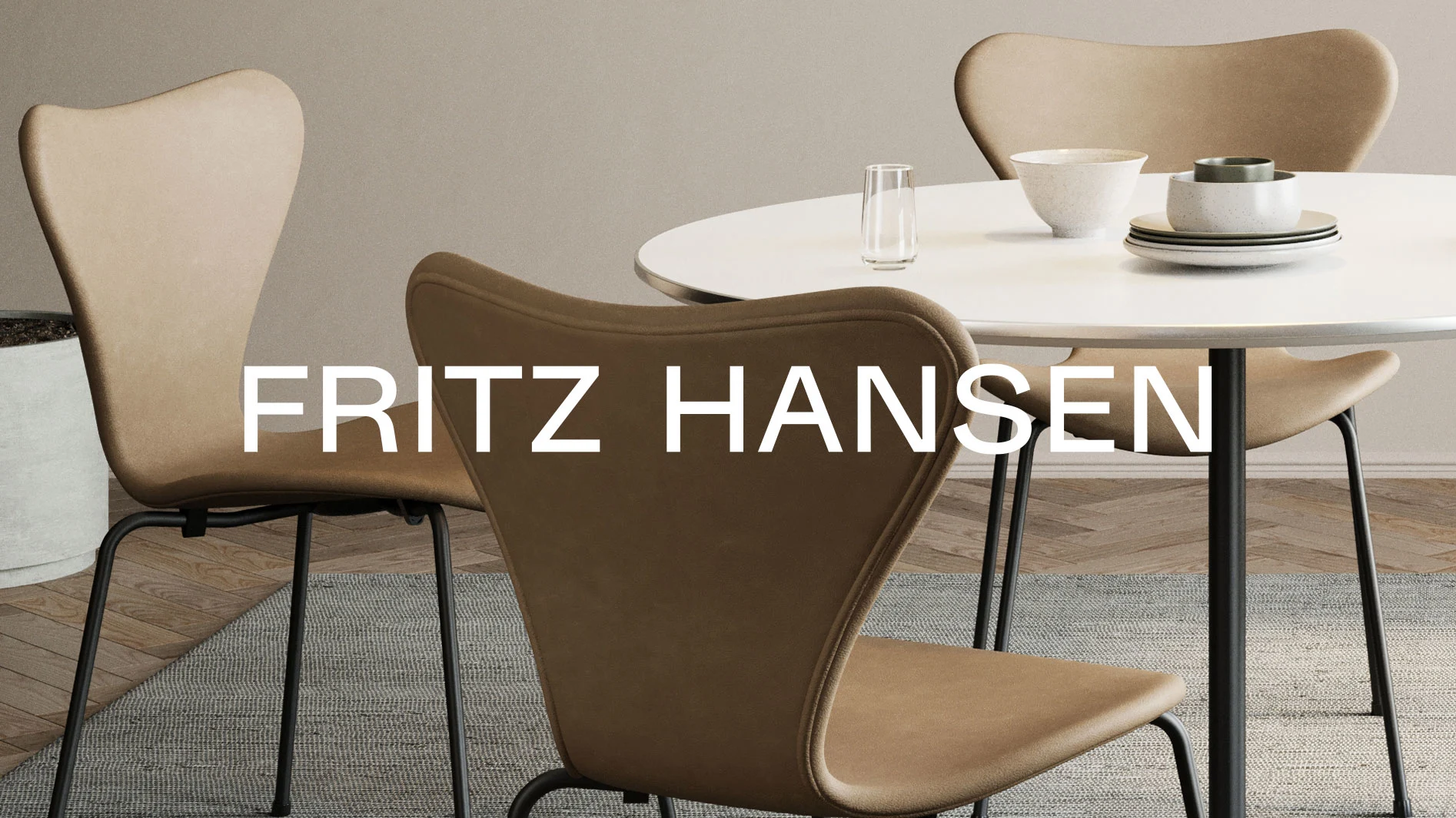 Ett runt vitt bord med fyra ljusbruna, klädda stolar med svarta ben. Texten 'FRITZ HANSEN' är synlig.