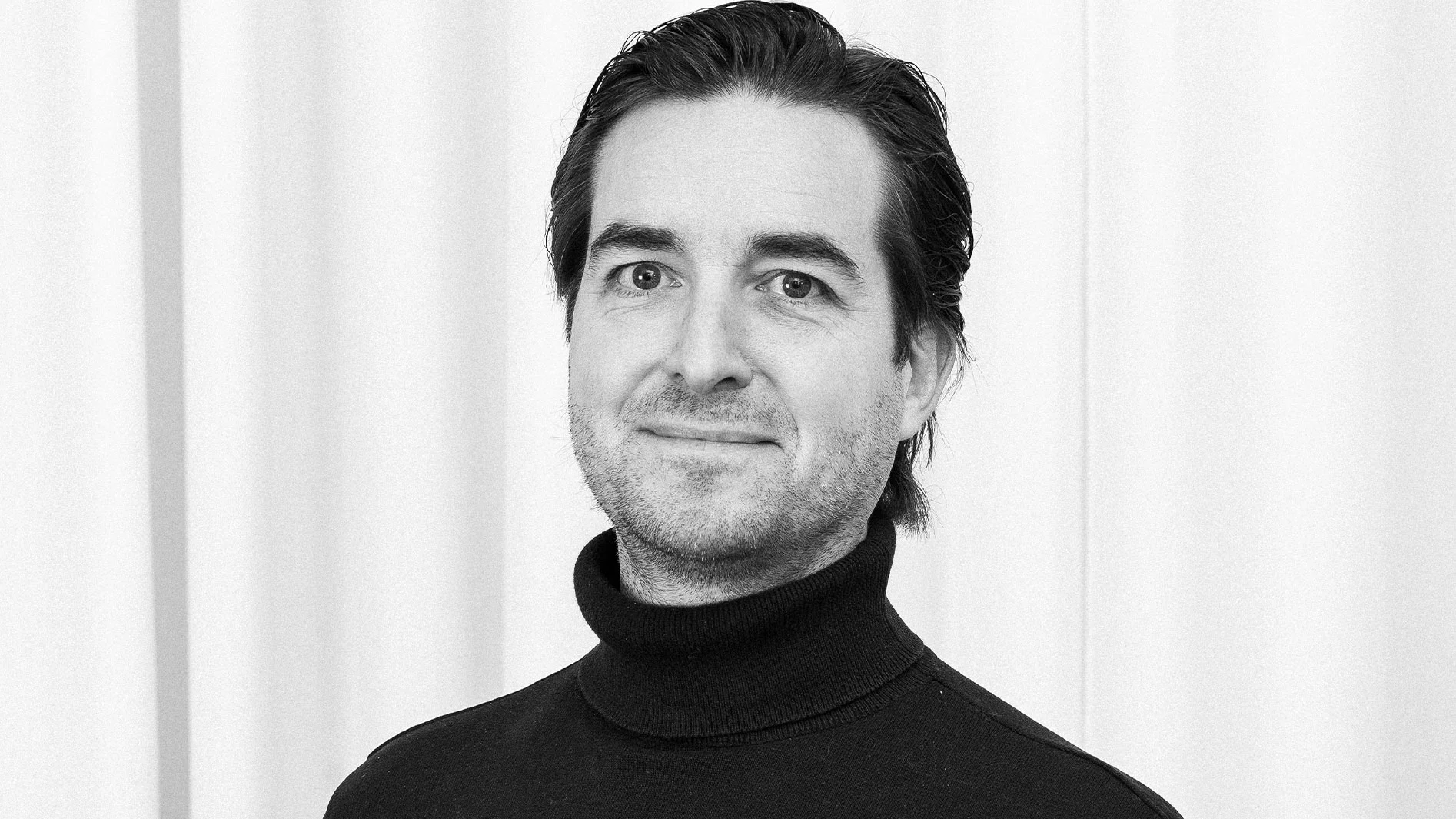 Svartvitt porträtt av en man med mörkt hår i en svart polotröja.