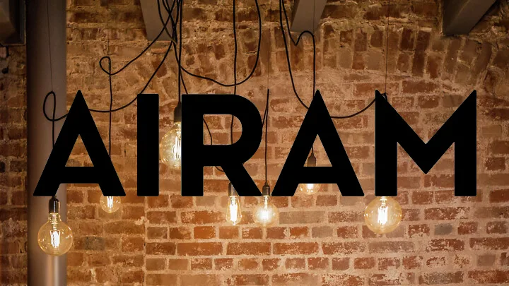 Svarta bokstäver som bildar ordet "AIRAM" framför en tegelvägg, med hängande vintage glödlampor.