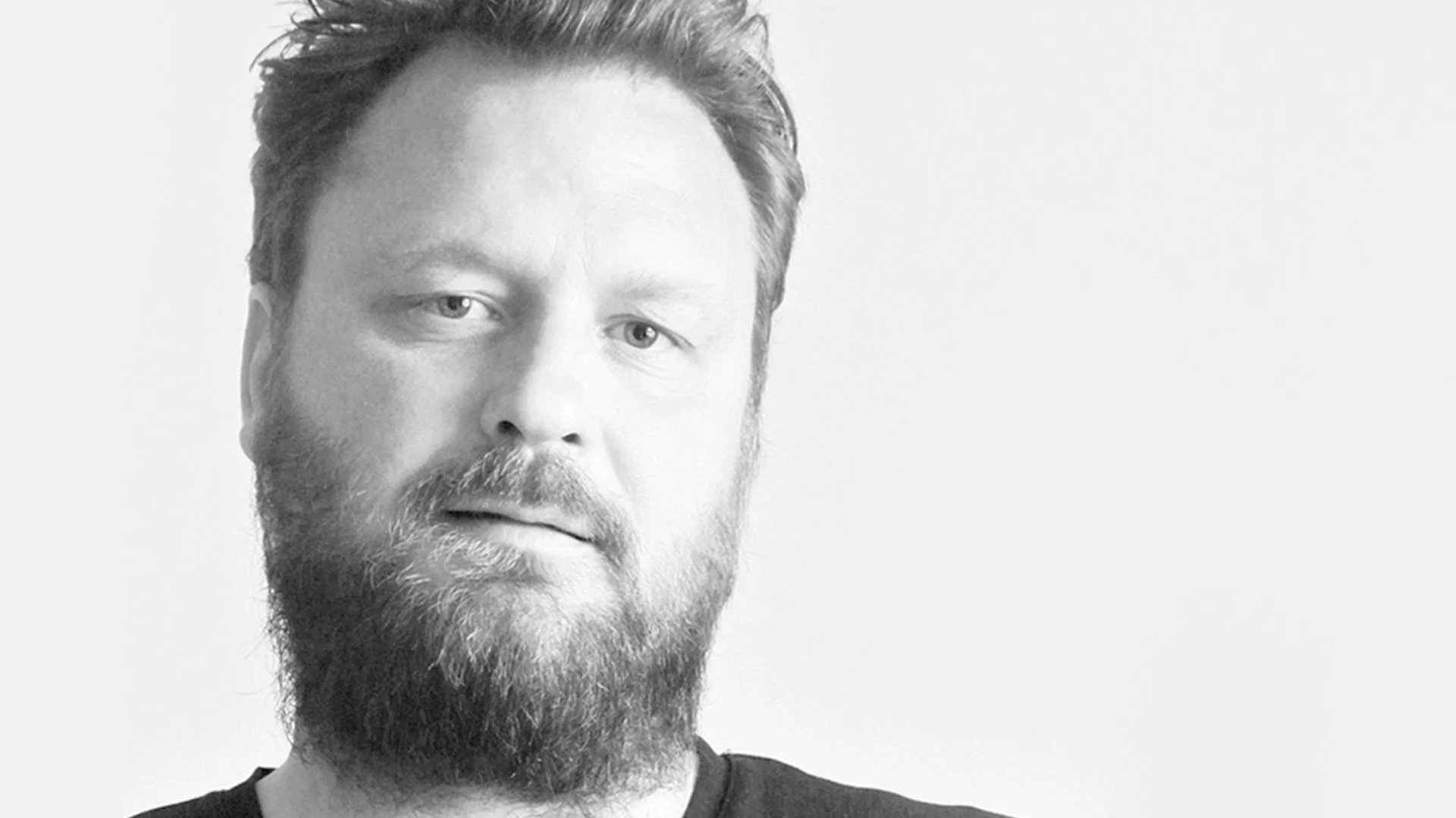 Svartvitt närbild av en skäggig man som tittar in i kameran.