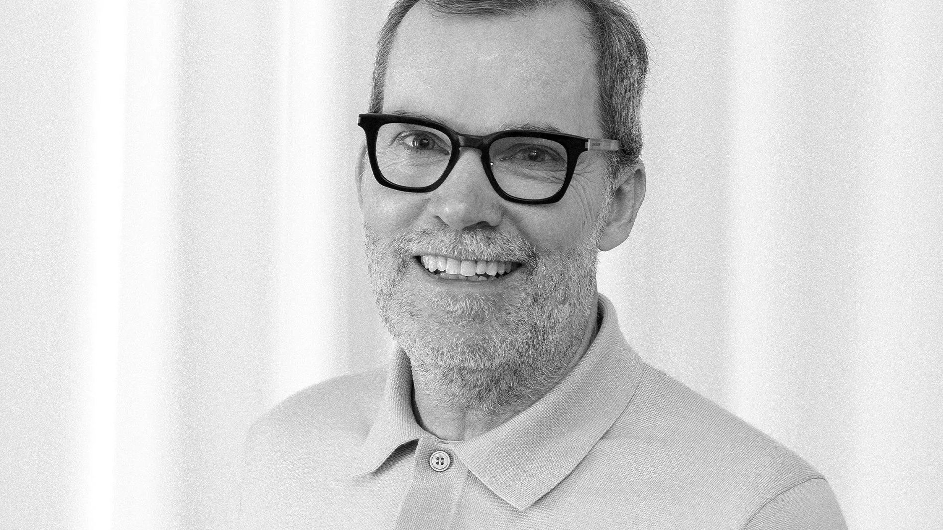 Svartvitt porträtt av en leende medelålders man med glasögon, skägg och kort grånande hår.