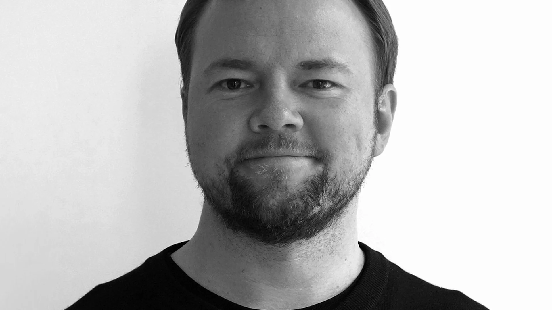 Svartvitt porträtt av en skäggig man som tittar rakt in i kameran.