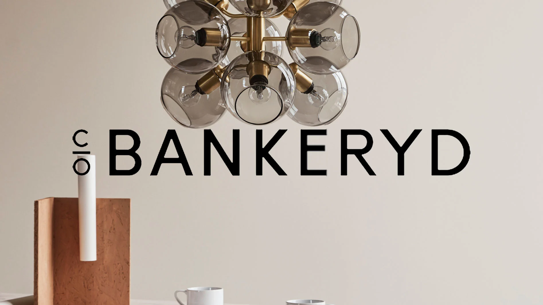 Modern ljuskrona med flera glaskupor och synliga glödlampor, med texten 'c/o BANKERYD'.