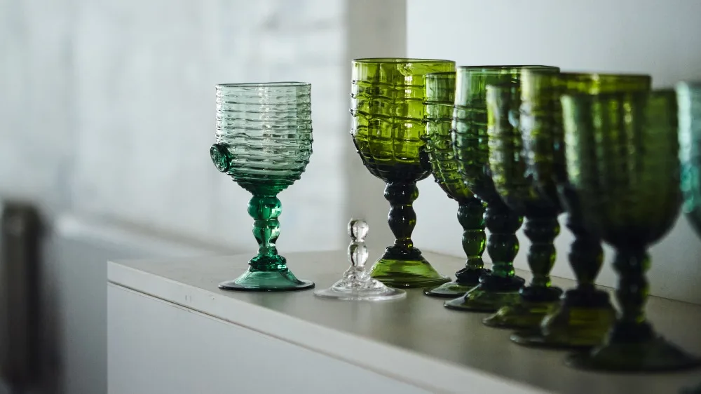 En rad gröna vinglas med räfflad textur och en liten klar glasdekoration.