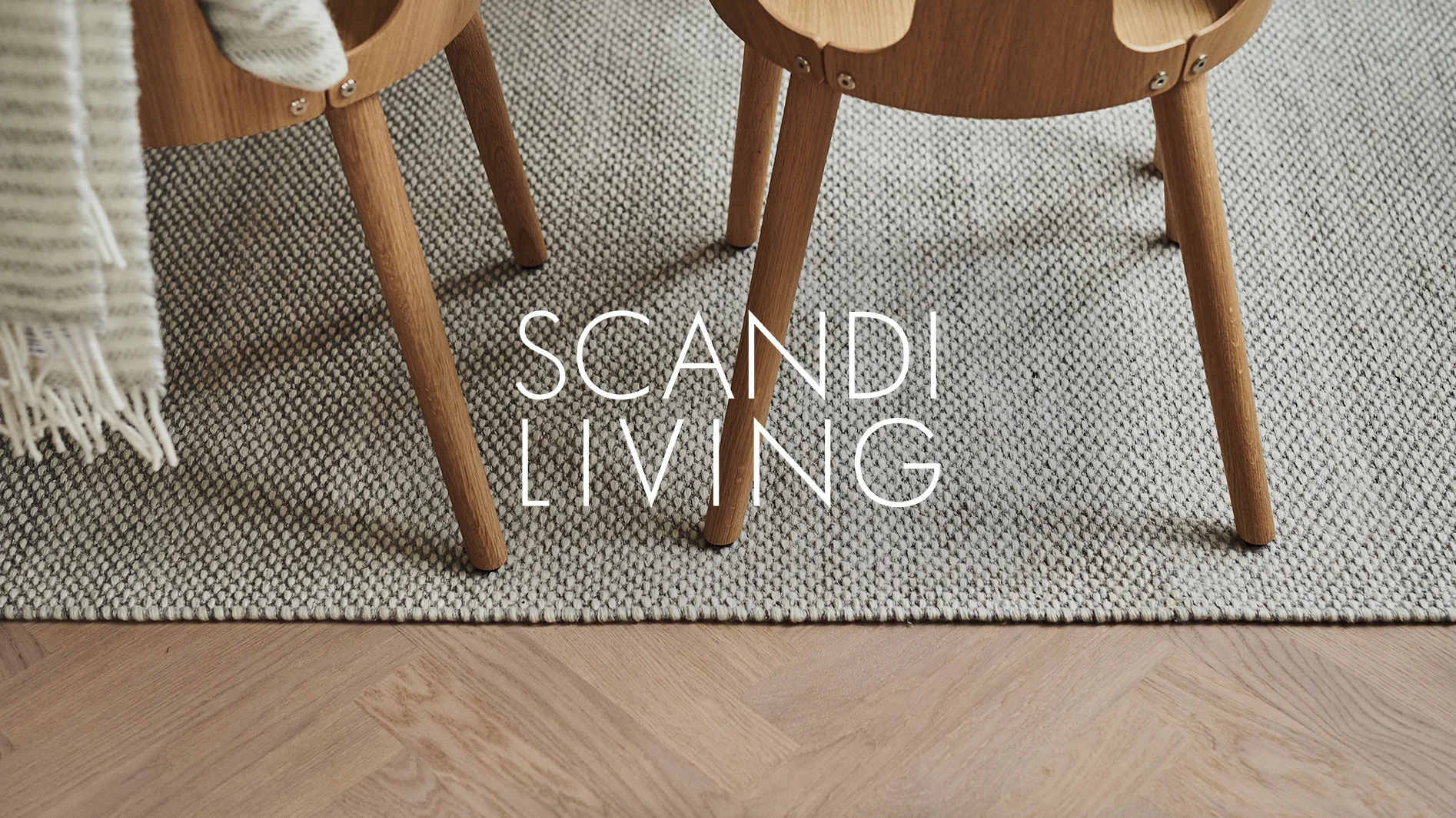 Närbild av två trästolsben på en grå, texturerad matta med en randig filt och parkettgolv. Text: SCANDI LIVING.