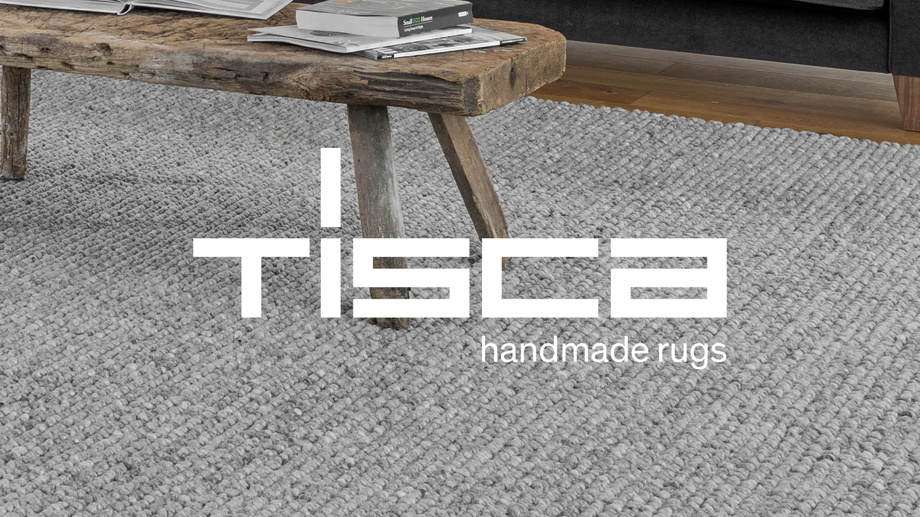 Ljusgrå, texturerad handgjord matta under ett rustikt bord på ett trägolv.