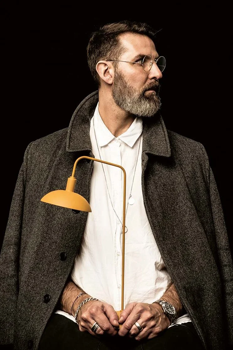 En man med skägg och glasögon håller en gul lampa.