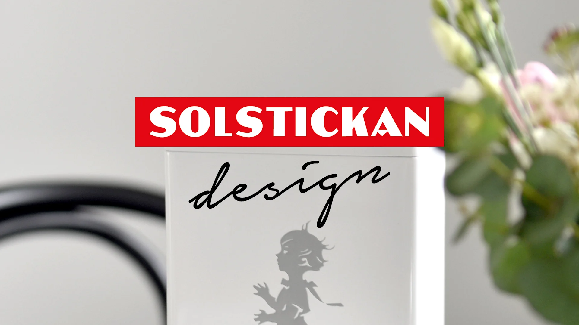 Vit föremål med röd «SOLSTICKAN»-logotyp, svart «design»-text och silhuett av ett barn.