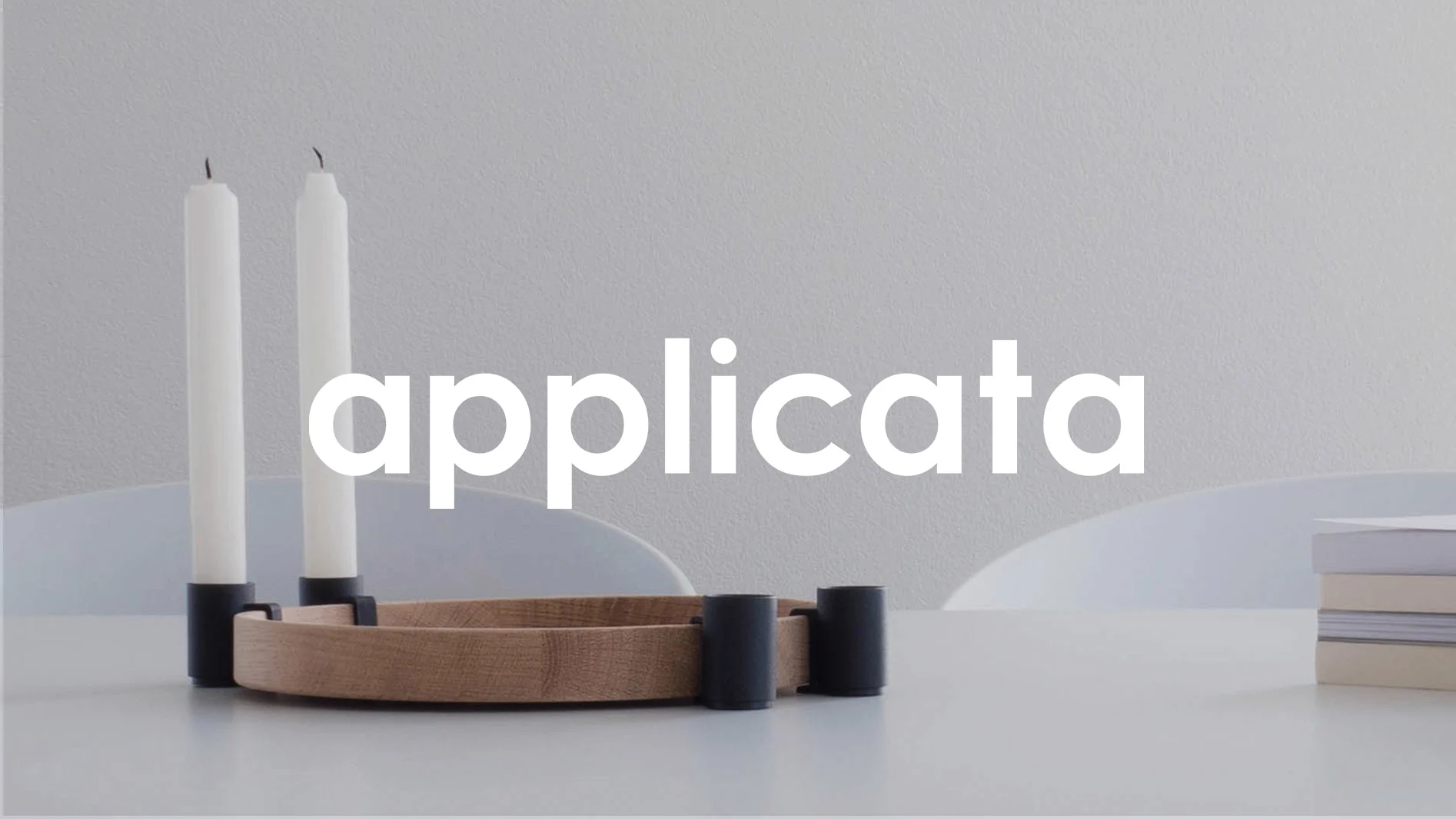 Två vita ljus i svarta hållare på en träbas med logotypen Applicata.
