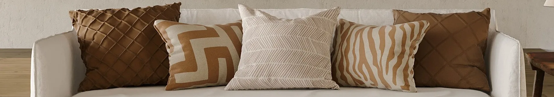Fem prydnadskuddar på vit soffa. Två bruna kviltade kuddar och tre beige/bruna kuddar med geometriska och randiga mönster.