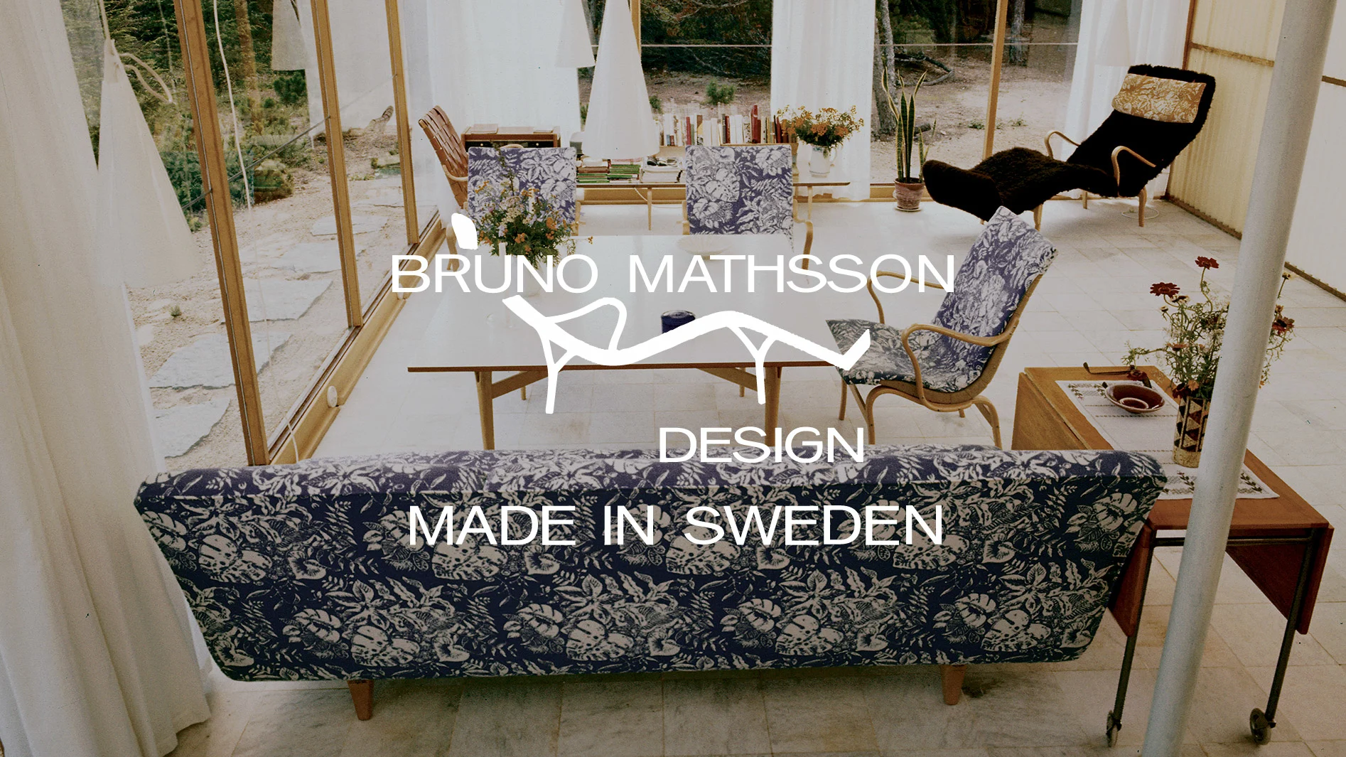 Rum med Bruno Mathsson-möbler: blåmönstrad soffa och stolar, mörk fåtölj. Text: Bruno Mathsson Design Made in Sweden.