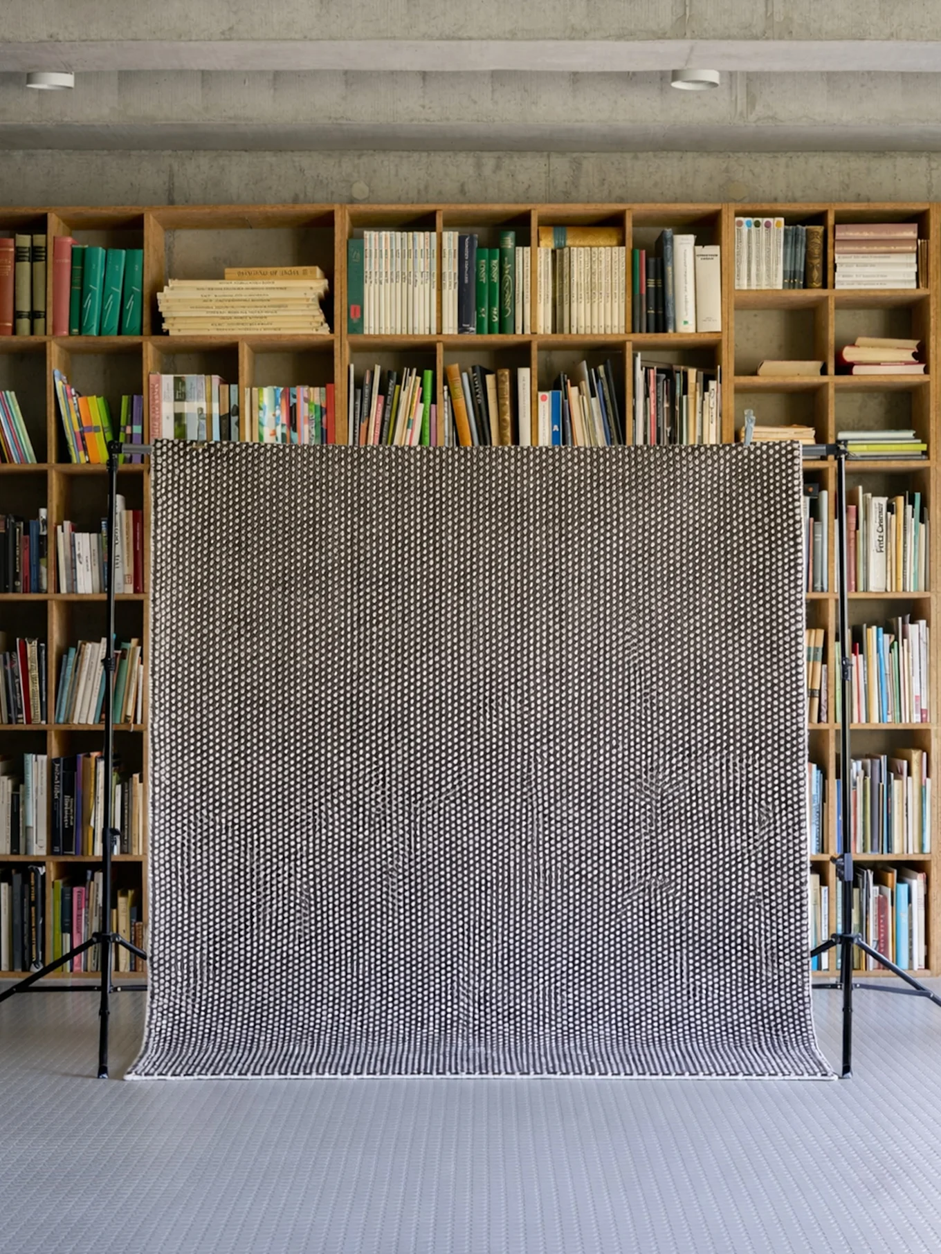 Svart och vitt prickigt matta draperat över ett stativ, med bokhyllor fyllda med böcker i bakgrunden.
