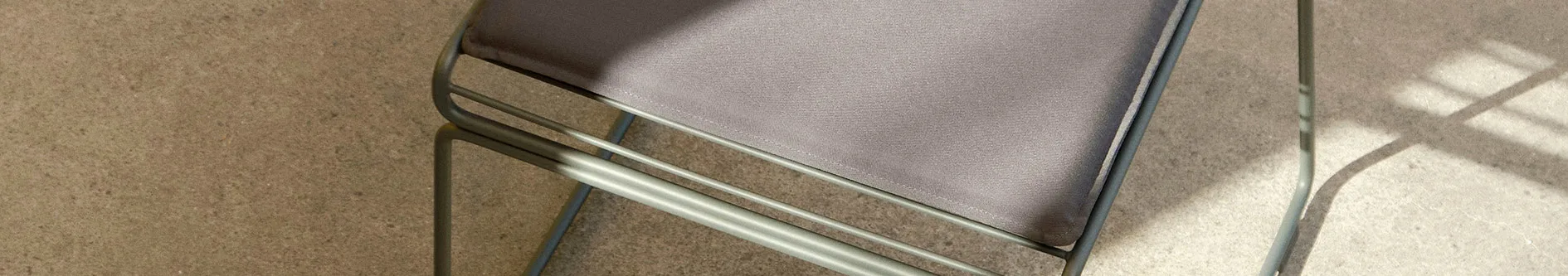Grå utomhusstol med tygsits på en texturerad ljusbrun yta, med skuggor.