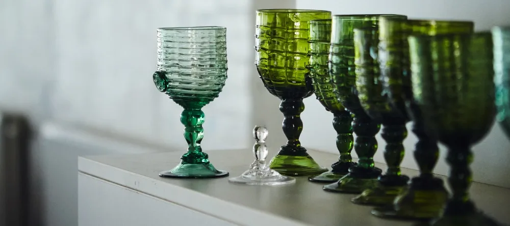 Gröna, räfflade glas med fot på rad på en vit yta.