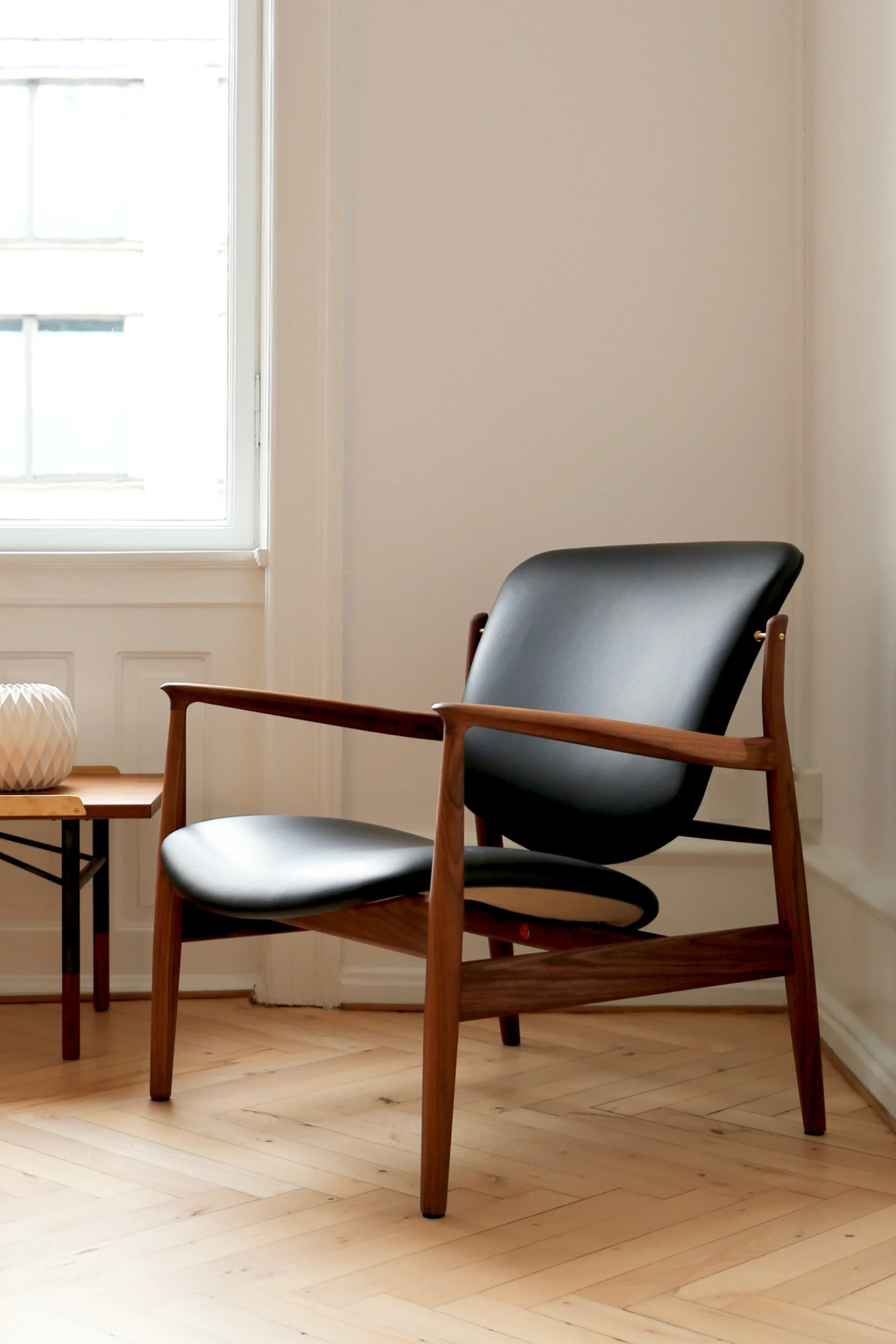 En modern loungestol med svart lädersits och rygg, och en träram, på ett ljust fiskbensparkettgolv.