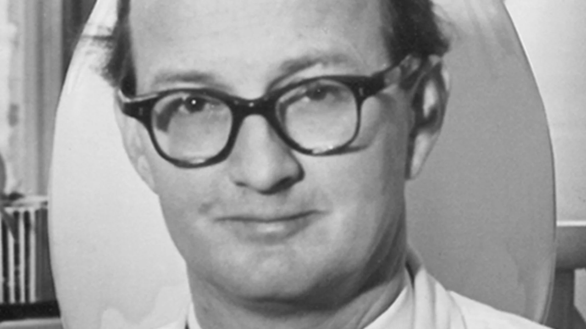 Svartvitt närbild på en man med glasögon som tittar mot kameran.