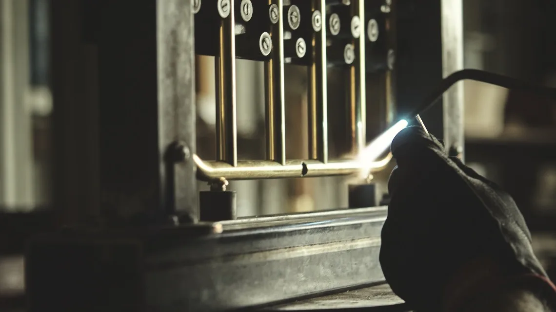 En handskbeklädd hand löder en mässingsfärgad metallram med vertikala stavar.