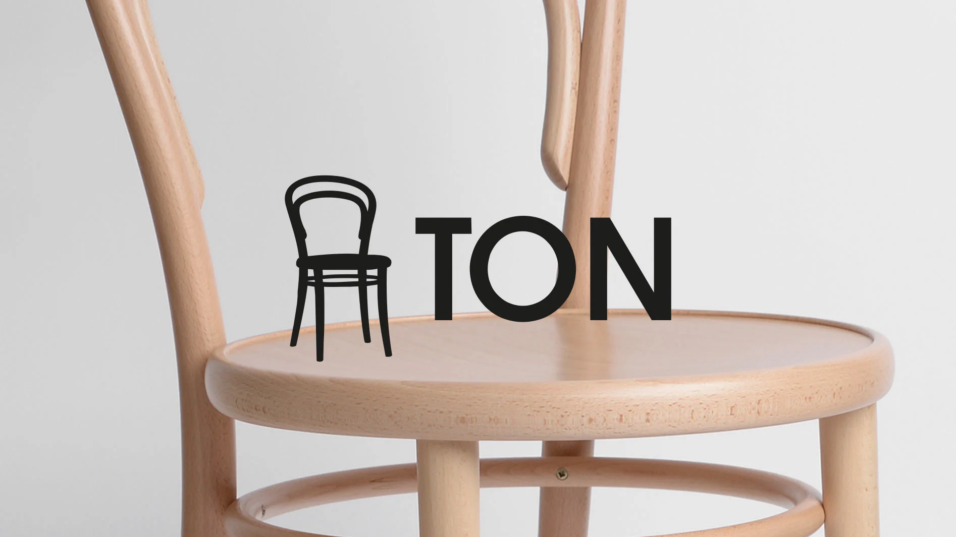 Ljus böjträstol med 'TON'-logotyp, där 'T':et är en svart stolsilhuett.