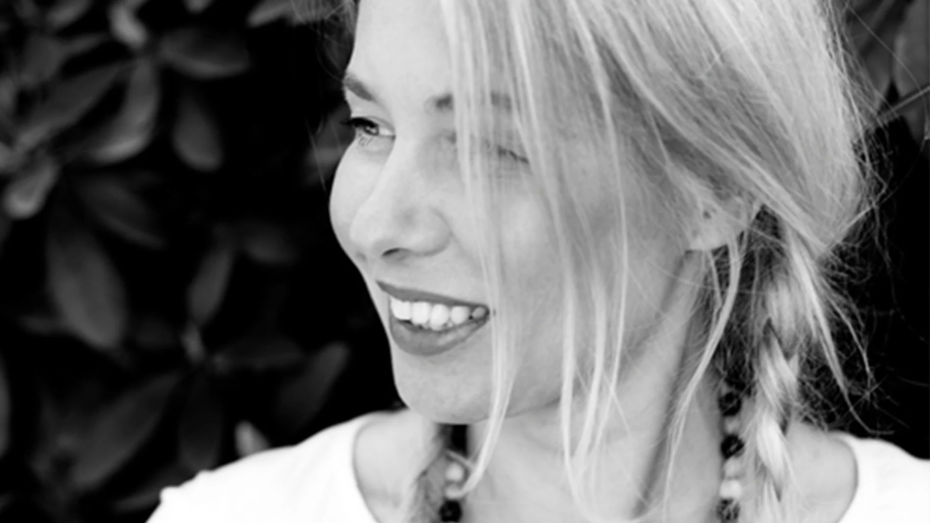 Svartvitt närbild av en leende kvinna med blont hår och en fläta, som tittar åt sidan.