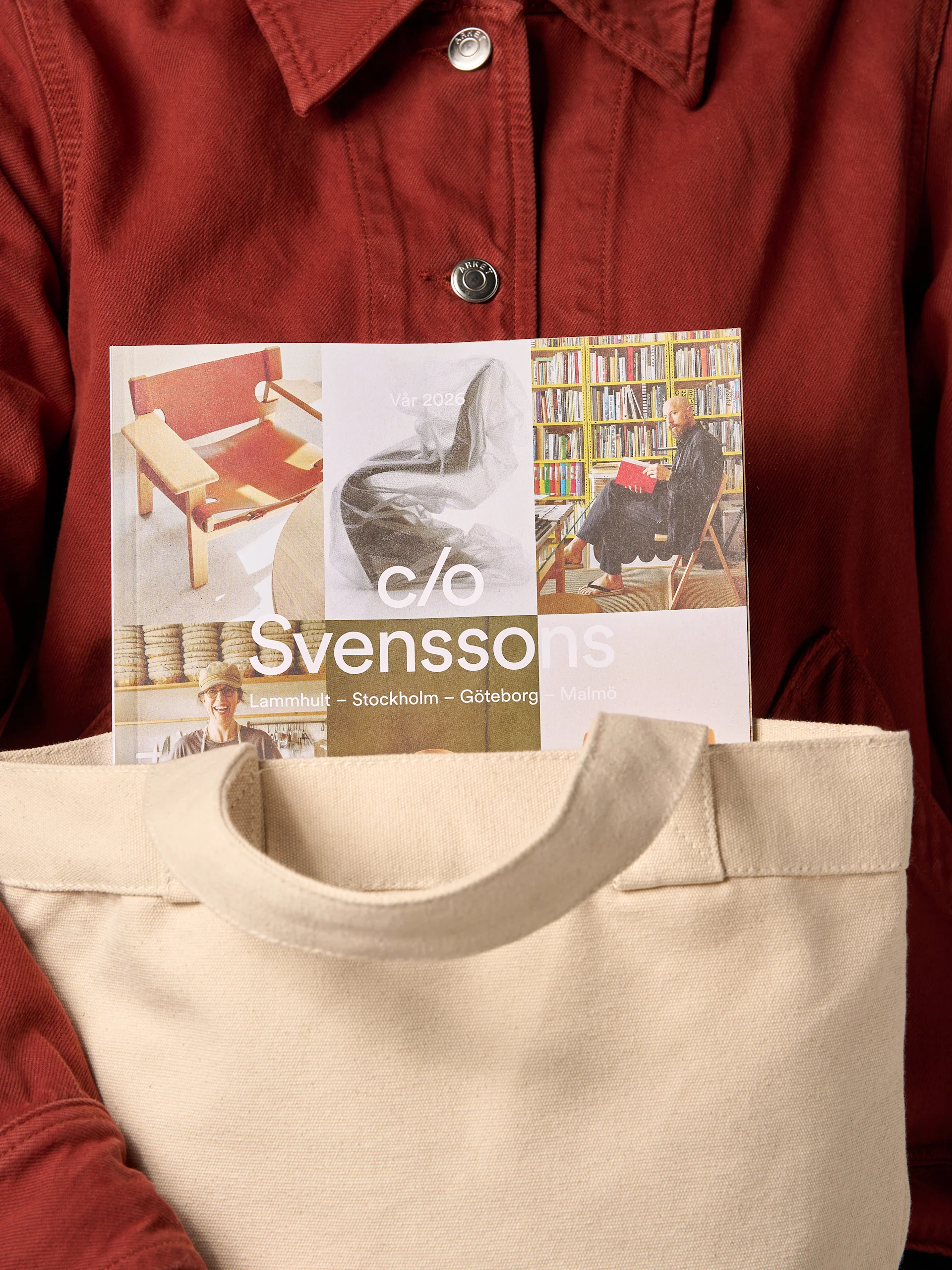 En person i röd jacka håller en beige tygväska med en "Svenssons"-tidning som sticker upp. Framsidan visar möbler och människor.