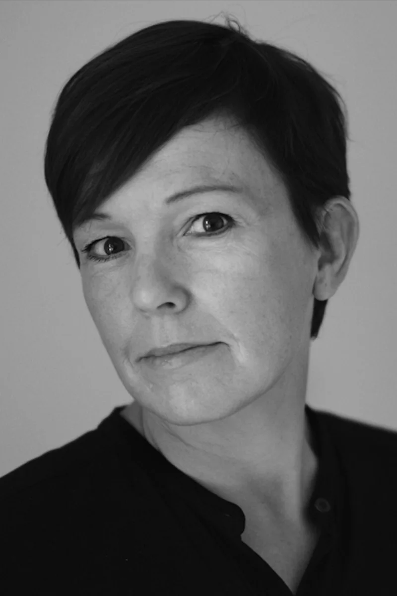 Svartvitt porträtt av en kvinna med kort, mörkt hår som tittar direkt in i kameran.