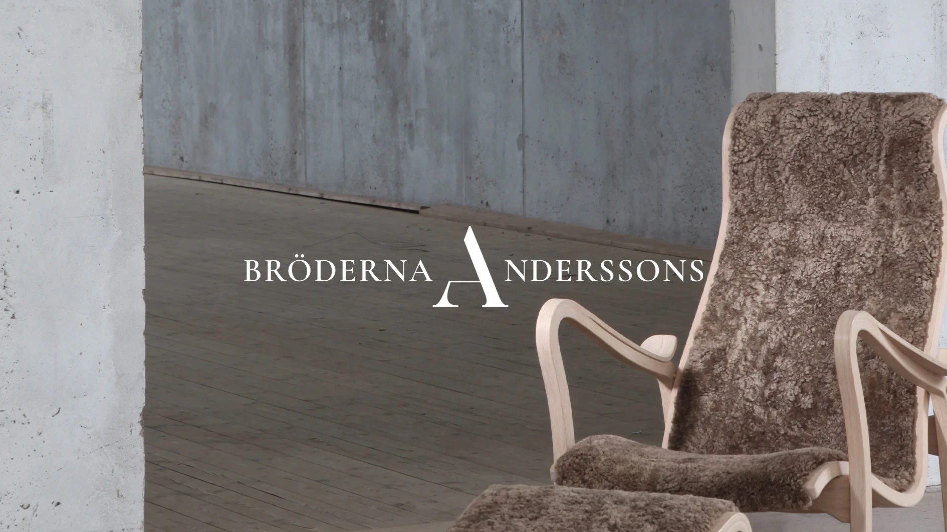 Bröderna Anderssons logotyp över en träfåtölj med brunt fårskinn och fotpall i ett rum med betongväggar.