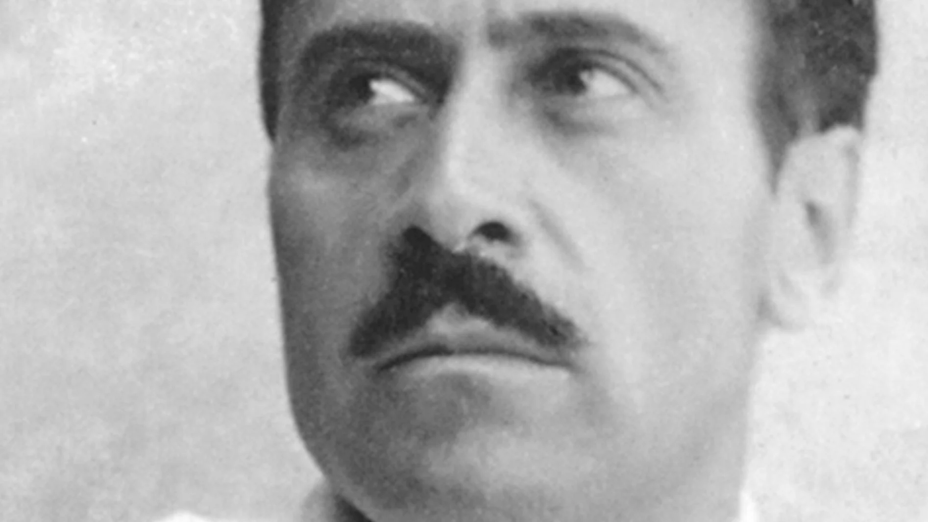 Svartvit närbild av en man med mörk mustasch, som tittar upp och åt höger.