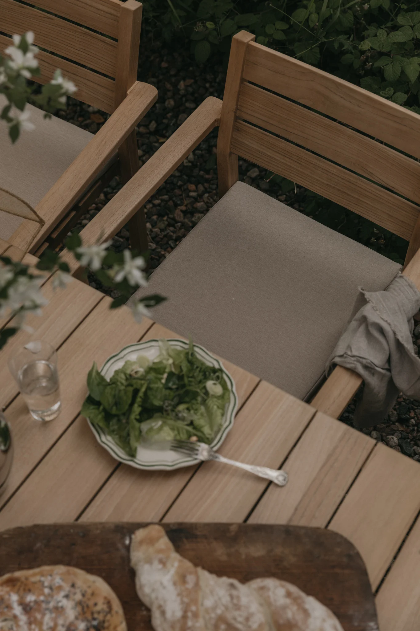 Utomhus matplats med träbord, stolar, en salladstallrik, ett glas vatten och bröd.