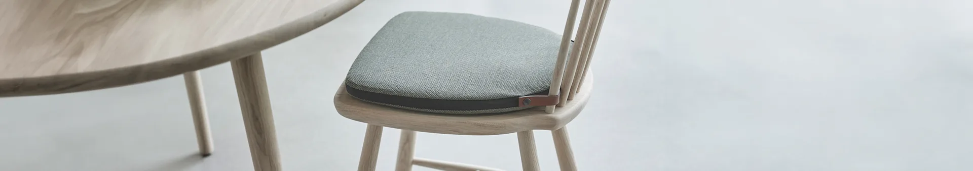 Närbild av ljust träbord och matchande stol med grön textil dyna och brun läderdetalj.