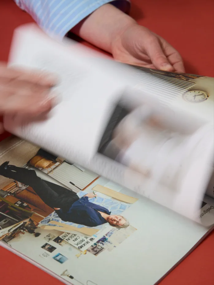 Händer bläddrar snabbt genom en tidning med en kvinna i blå skjorta på en sida, mot en röd bakgrund.