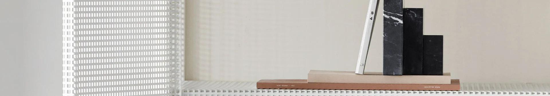 En stapel böcker och mörka marmorblock på en vit galleryta, med en geometrisk skugga på väggen.