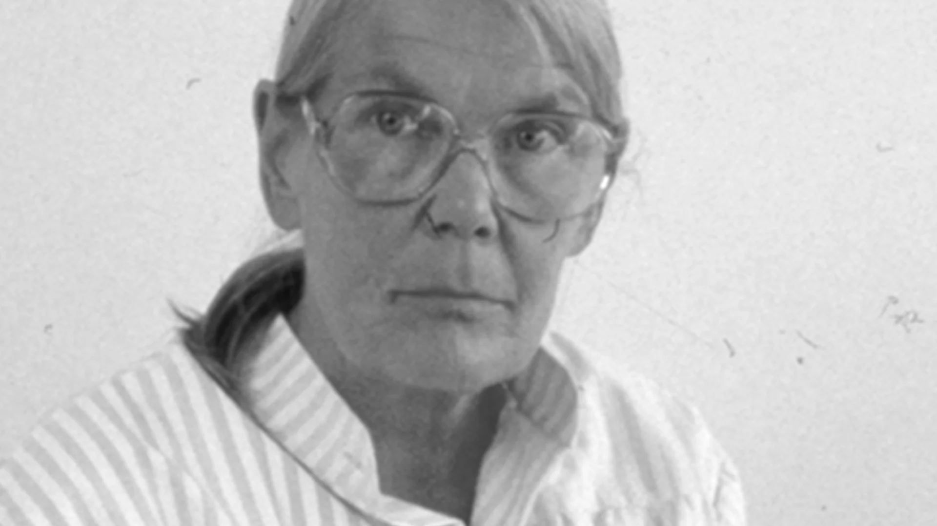 Svartvitt porträtt av en äldre kvinna med glasögon och randig skjorta, som tittar rakt fram.