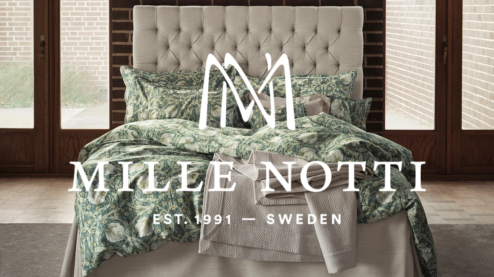 En säng med tuftad sänggavel och sängkläder med grönt och vitt blommönster, med en beige quiltad filt.