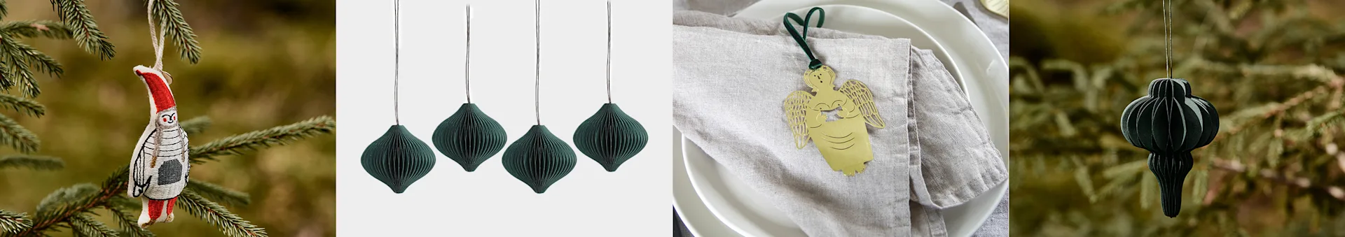 Juldekorationer: en broderad fågel, mörkgröna pappersornament och en guldfärgad ängel.