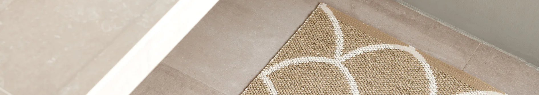 Närbild av en flätad matta i beige med vita vågiga linjer på ett klinkergolv.